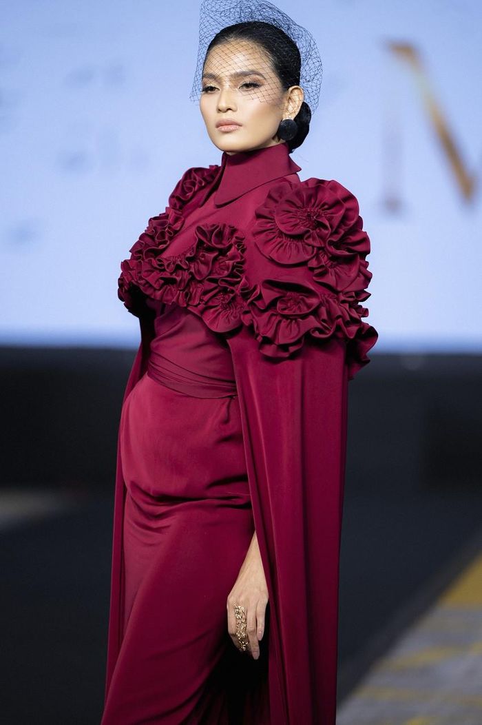 Á hậu Trương Thị May xuất hiện mở màn trong BST "Muse - Thì thầm" với thiết kế dạ hội màu đỏ mận. Điểm nhấn của bộ trang phục chính là phần váy lụa dài xẻ và áo choàng kết hoa 3D, phụ kiện đi kèm là lưới đội đầu toát lên vẻ sang trọng, quyến rũ.